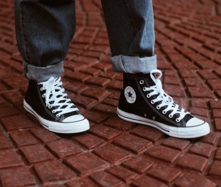 Beine eines Mannes in Jeans und dunkelblauen Converse Schuhen auf gepflasterter Straße