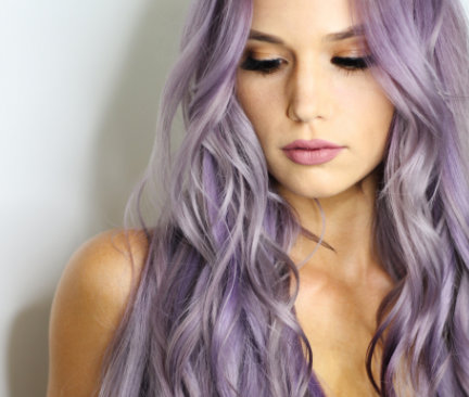 junge Frau mit pastelllila gefärbten und gewellten Haaren, die verträumt nach unten schaut