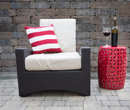 Sessel aus schwarzem Rattan mit weißer Sitzauflage neben einem rotem Beistelltisch auf Steinterrasse