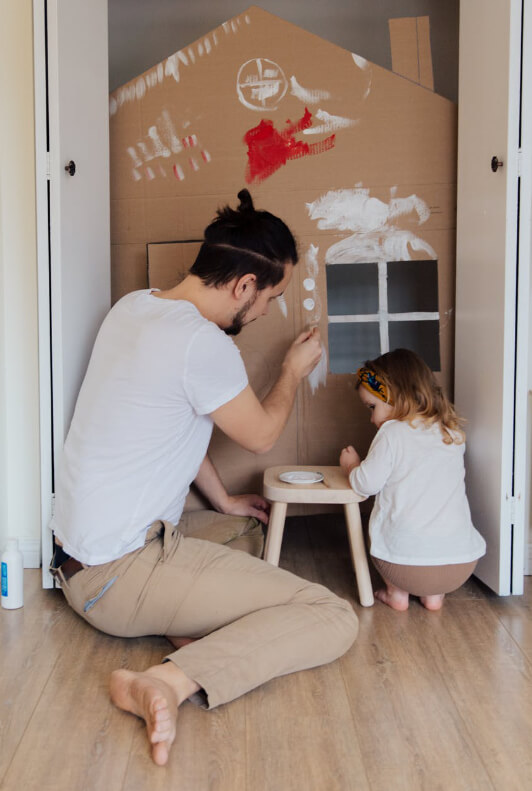 Vater und Kind bauen gemeinsam ein Haus aus Pappe und bemalen es mit bunter Farbe